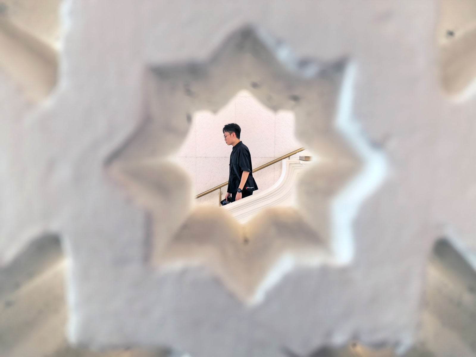A man in black walks past a cream wall, seen through a star-shaped opening in a decorative structure.