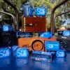 Several CineStill 50D Daylight film boxes are arranged among vintage and toy cameras outdoors, with trees and sunlight in the background.