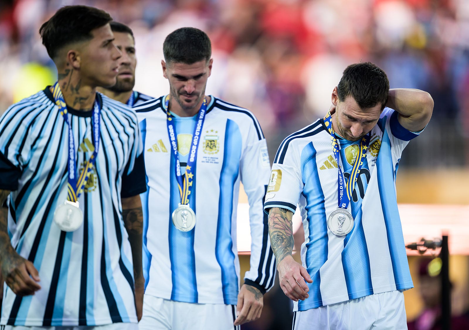 Four soccer players in blue and white striped jerseys, wearing silver medals, walk off the field looking disappointed after a match.
