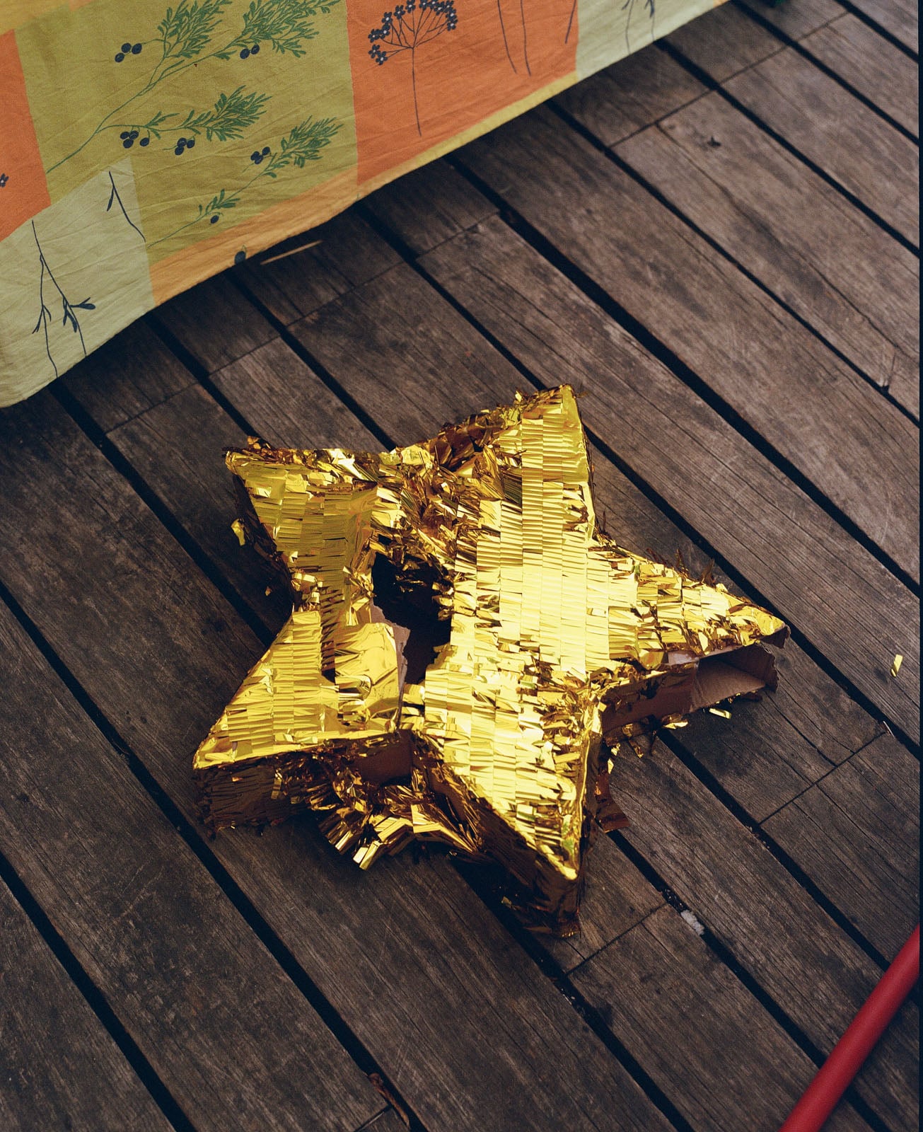 A gold, star-shaped piñata with a hole in its center rests on a wooden deck next to a patterned fabric.
