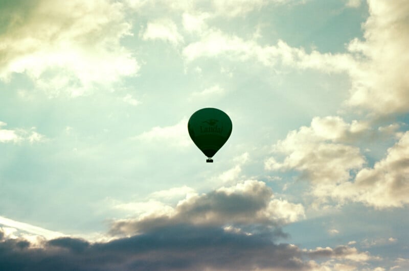 A hot air balloon with the word "Landal" floats in a bright, partly cloudy sky, silhouetted against the sunlight and surrounded by fluffy clouds.