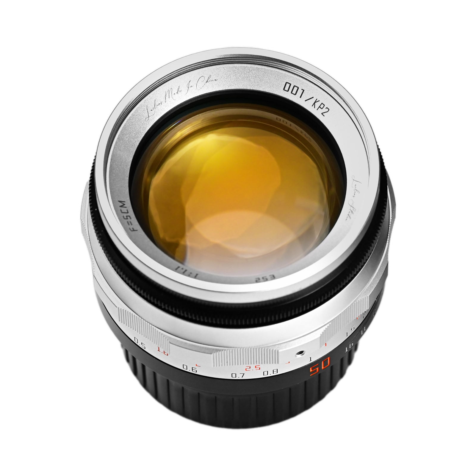 A close-up view of a camera lens with a silver and black body, yellowish glass, and engraved markings around the rim including numbers and letters. The focus and aperture rings are visible.