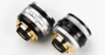 Two camera lenses with metallic finishes—one silver and gold, the other black and gold—are placed side by side on a white surface. Both feature red, white, and black markings and numbers.
