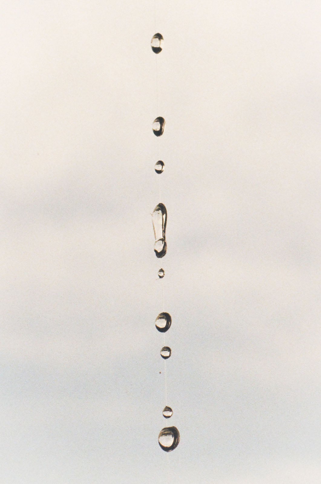 A vertical string of water droplets suspended against a pale, overcast sky.