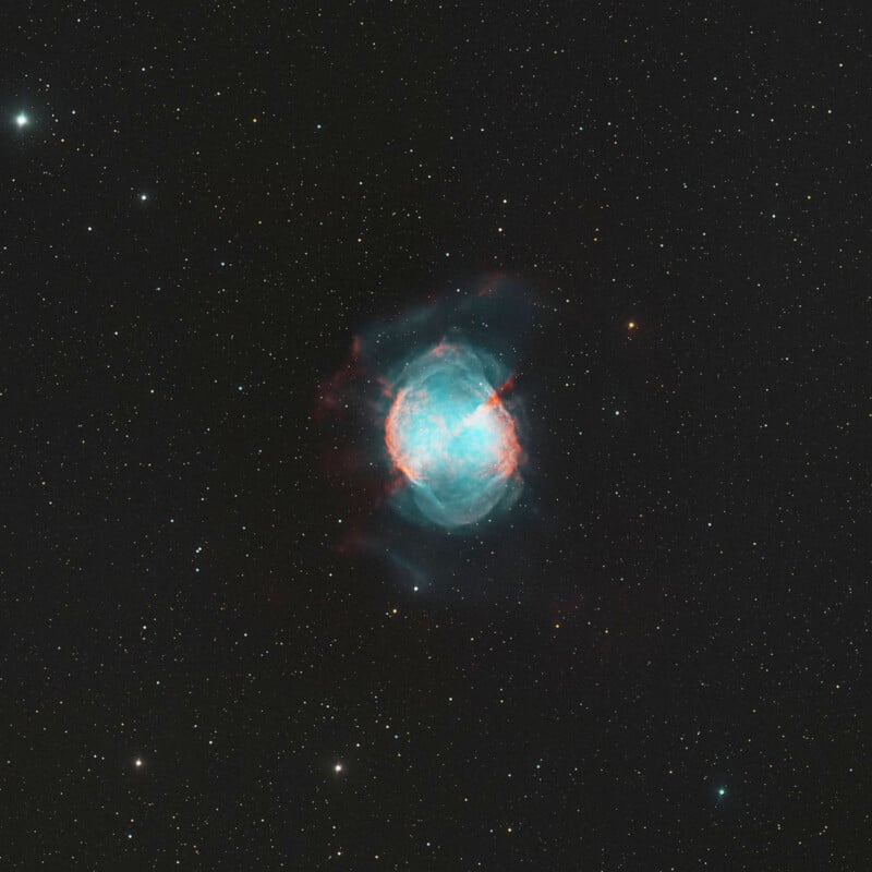 A glowing, turquoise and red planetary nebula sits centered against a vast field of distant stars in deep space.
