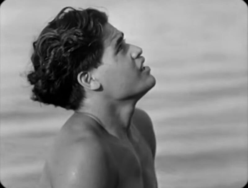 A young man with wet hair looks upward while standing in water, shown in black and white.