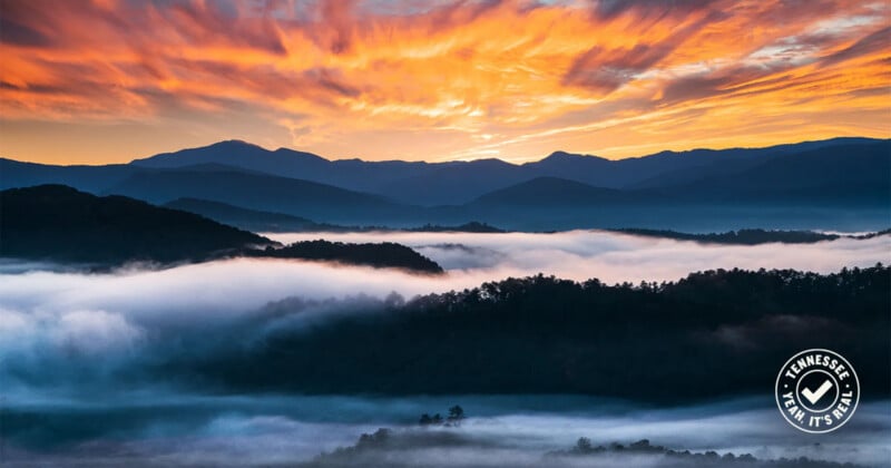 Colorful sunrise sky with dramatic orange clouds above misty mountains and forested hills; fog blankets the valleys. A 