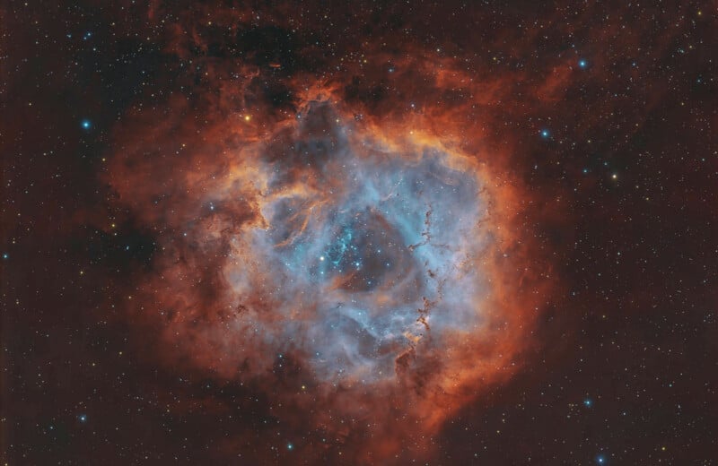 A vibrant nebula glows with deep red and orange outer clouds surrounding a bright, blue-tinted center filled with stars.