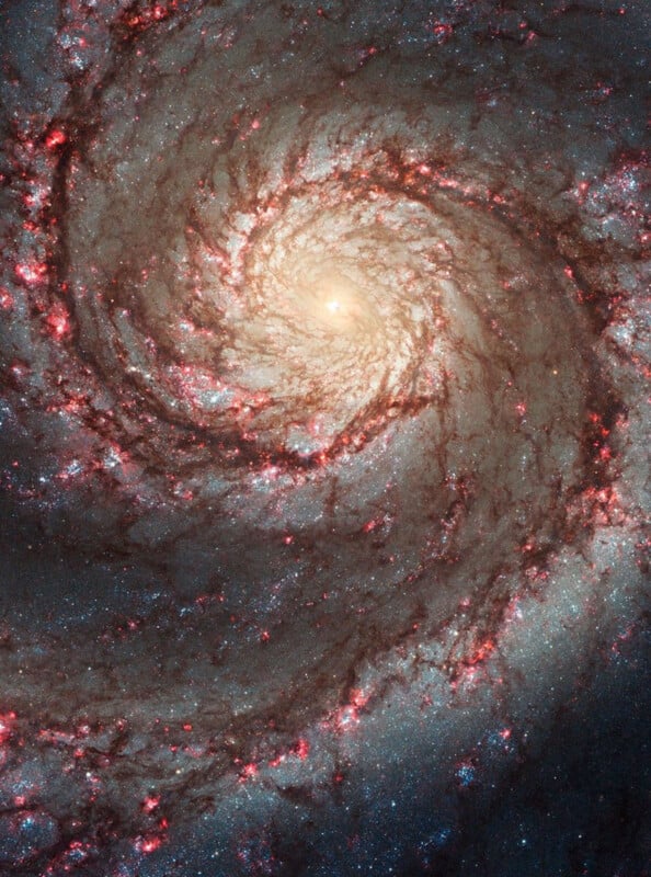 A detailed spiral galaxy with a bright yellow center, swirling arms, red star-forming regions, and blue clusters of stars set against the dark backdrop of space.