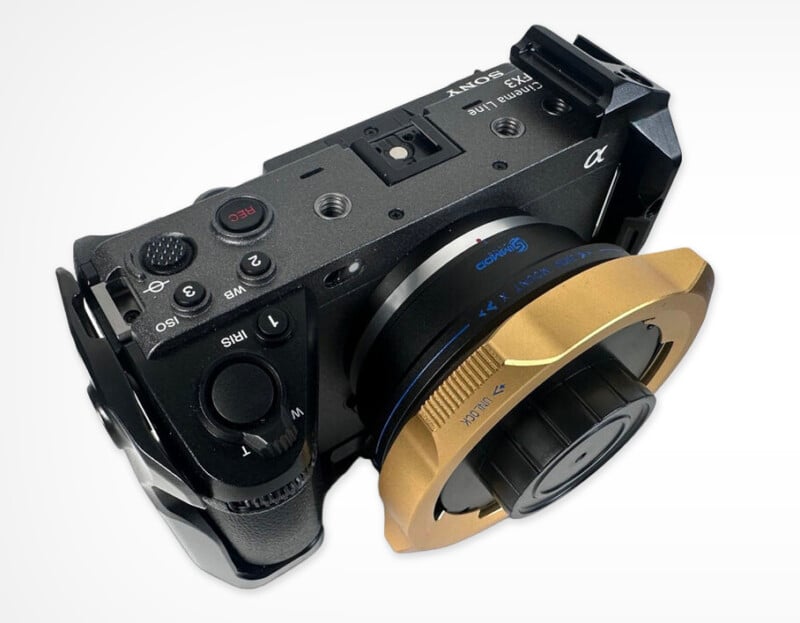 A Sony FX3 Cinema Line camera body viewed from above, featuring a gold-colored lens mount adapter with a black lens cap attached.