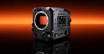 A black Fujifilm digital cinema camera body is displayed on a reflective surface with an orange to black gradient background. The camera features multiple dials, buttons, and a digital screen on its side.