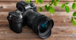 A Nikon Z7 II camera with a large lens rests on a wooden surface next to green leafy branches.