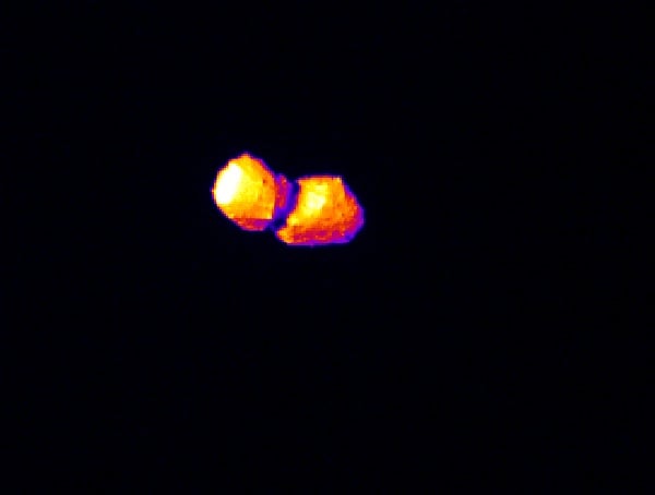 Two bright, irregularly shaped objects with orange and yellow hues appear against a completely black background, resembling glowing stones or celestial bodies.