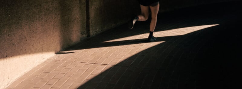 A person in shorts is running on a brick path partially lit by sunlight, with only their legs visible in the frame.