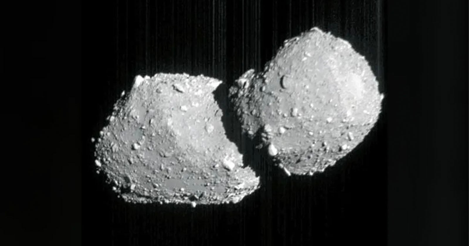 A grayscale image shows two rocky, irregularly shaped asteroids or space objects floating close together against a dark background, resembling a contact binary or two joined celestial bodies.