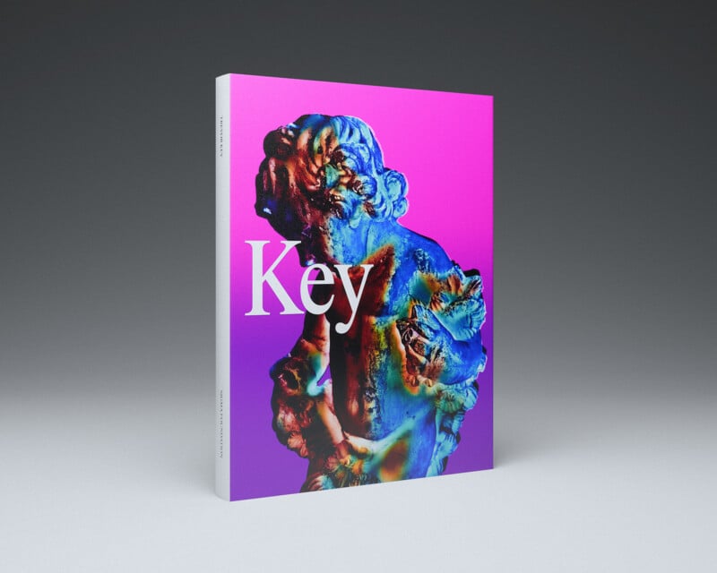 A book titled "Key" stands upright. The cover features a colorful, abstract sculpture of a classical figure against a pink and purple gradient background. The spine and cover display the title and subtle text details.