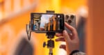 A hand holds a smartphone mounted on a tripod, with a Viltrox external monitor attached to the phone displaying a live camera feed of a street scene.