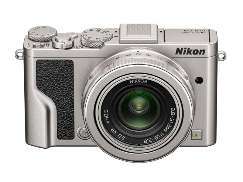 Silver Nikon digital camera with a large lens, textured black grip, dials on top, and the Nikon logo above the lens. The camera is photographed against a white background.