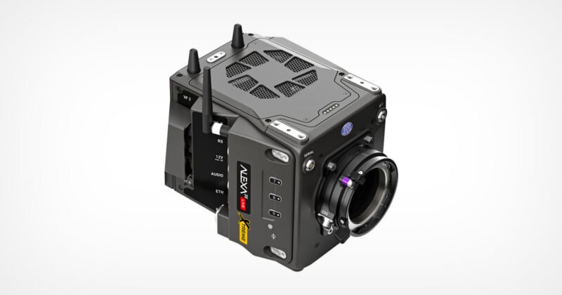 A black, box-shaped professional digital cinema camera with multiple buttons, ports, cooling vents, antennas, and a lens mount, shown on a plain white background.