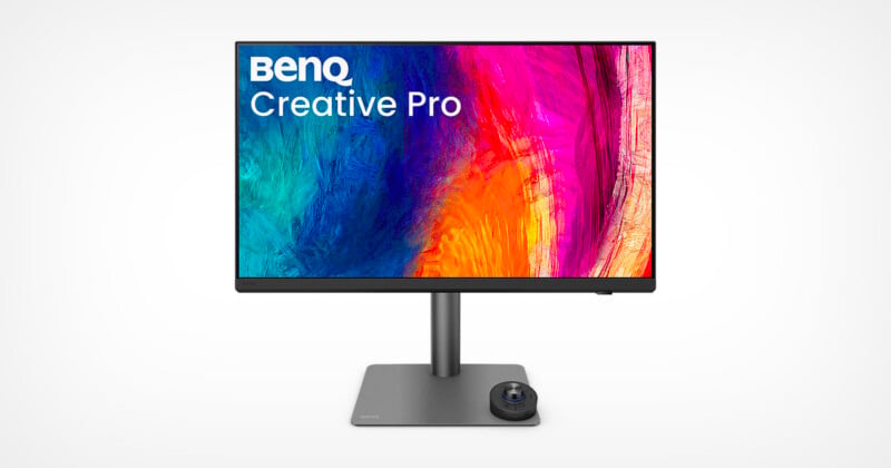 A BenQ Creative Pro monitor displays a vibrant, abstract multicolored design on the screen. The monitor is mounted on a sleek, minimalist stand with a circular control dial at the base.