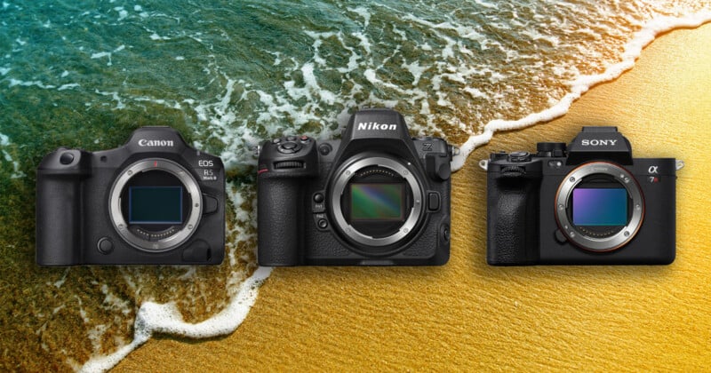 Three mirrorless cameras—Canon, Nikon, and Sony—are displayed side by side on a sandy beach with ocean waves in the background.