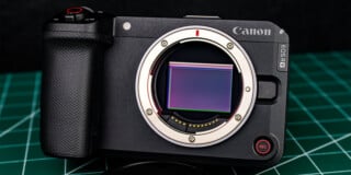 A Canon EOS RM mirrorless camera body with its lens removed, showing the sensor, placed on a green cutting mat background.