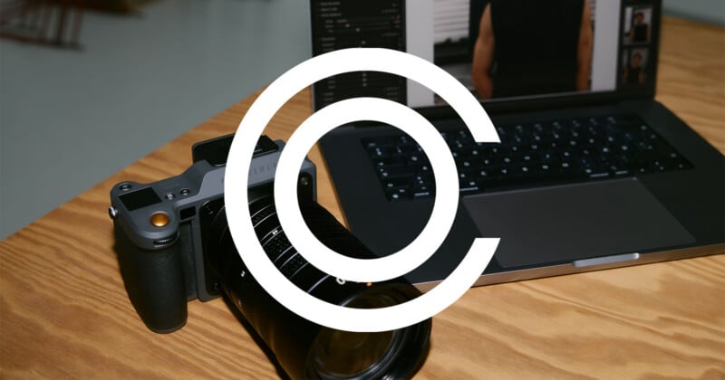 A digital camera rests on a wooden table next to an open laptop displaying photo editing software. A large white copyright symbol overlays the image, partially obscuring the view.