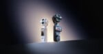 Two DJI Osmo handheld gimbal cameras, one white and one black, stand upright on a flat surface against a dark, gradient background.