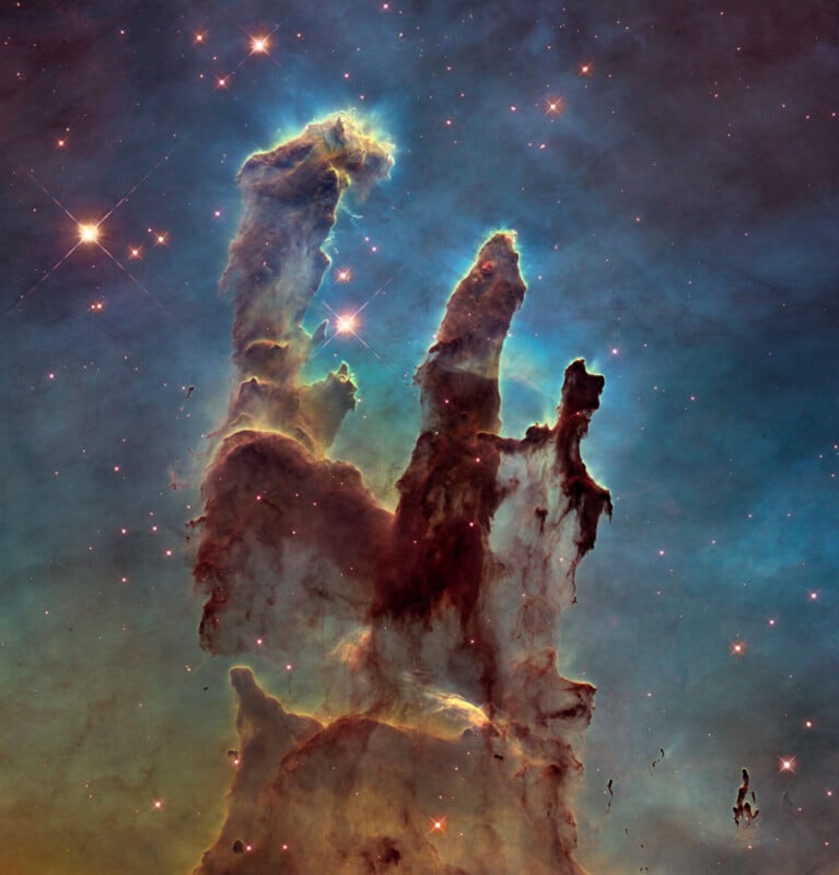 Tall, dark pillars of interstellar gas and dust rise against a colorful background of stars in the Eagle Nebula’s Pillars of Creation, photographed by the Hubble Space Telescope.