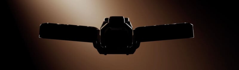 A dark, backlit silhouette of a mechanical device with two wide, rectangular wings extending from a central body.