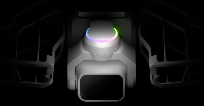 A close-up, centered view of a drone camera gimbal with a glowing, multi-colored LED ring, flanked by two dark, structural components.