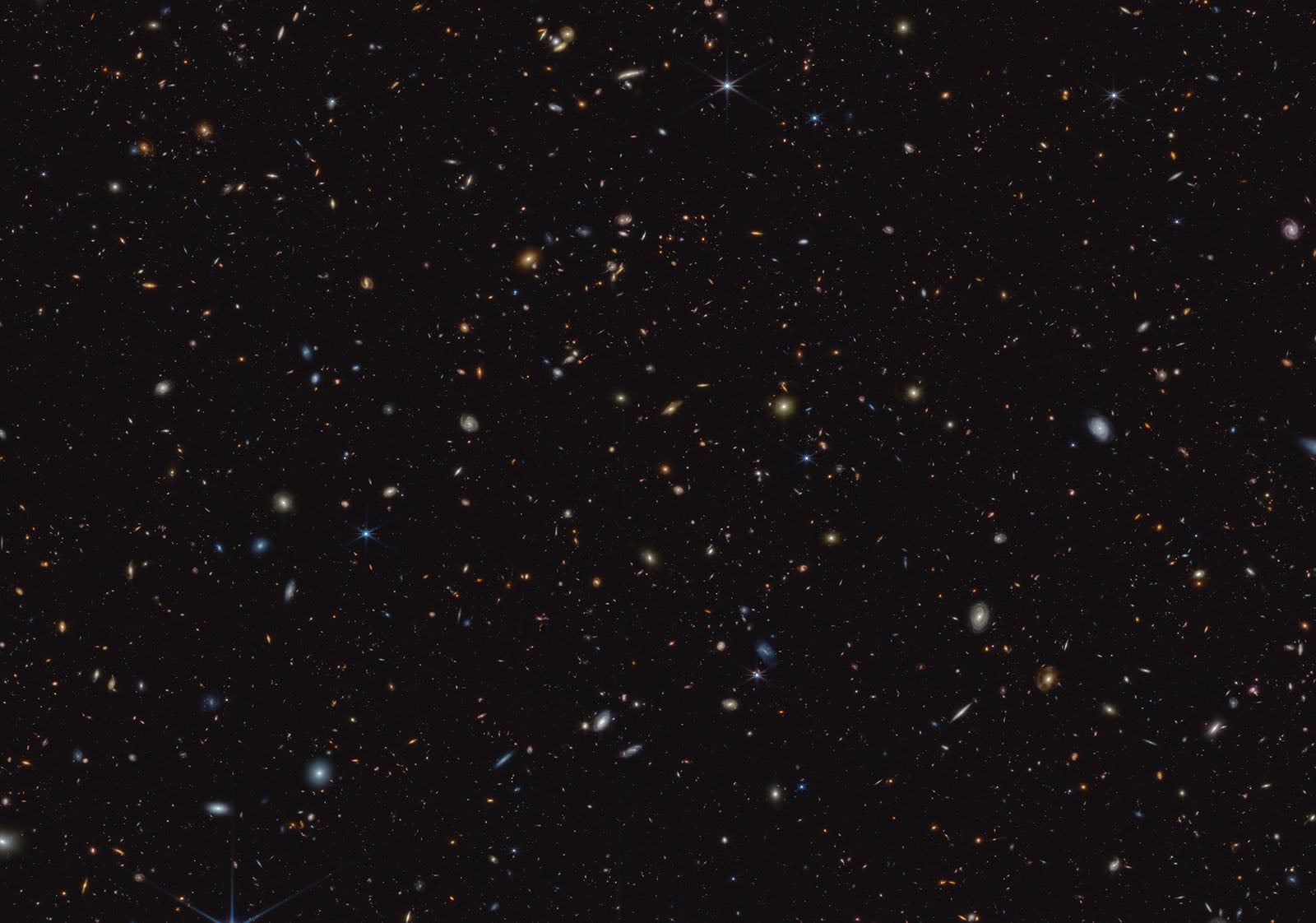 A deep space image showing countless distant galaxies, stars, and cosmic objects scattered across a dark, star-filled background.