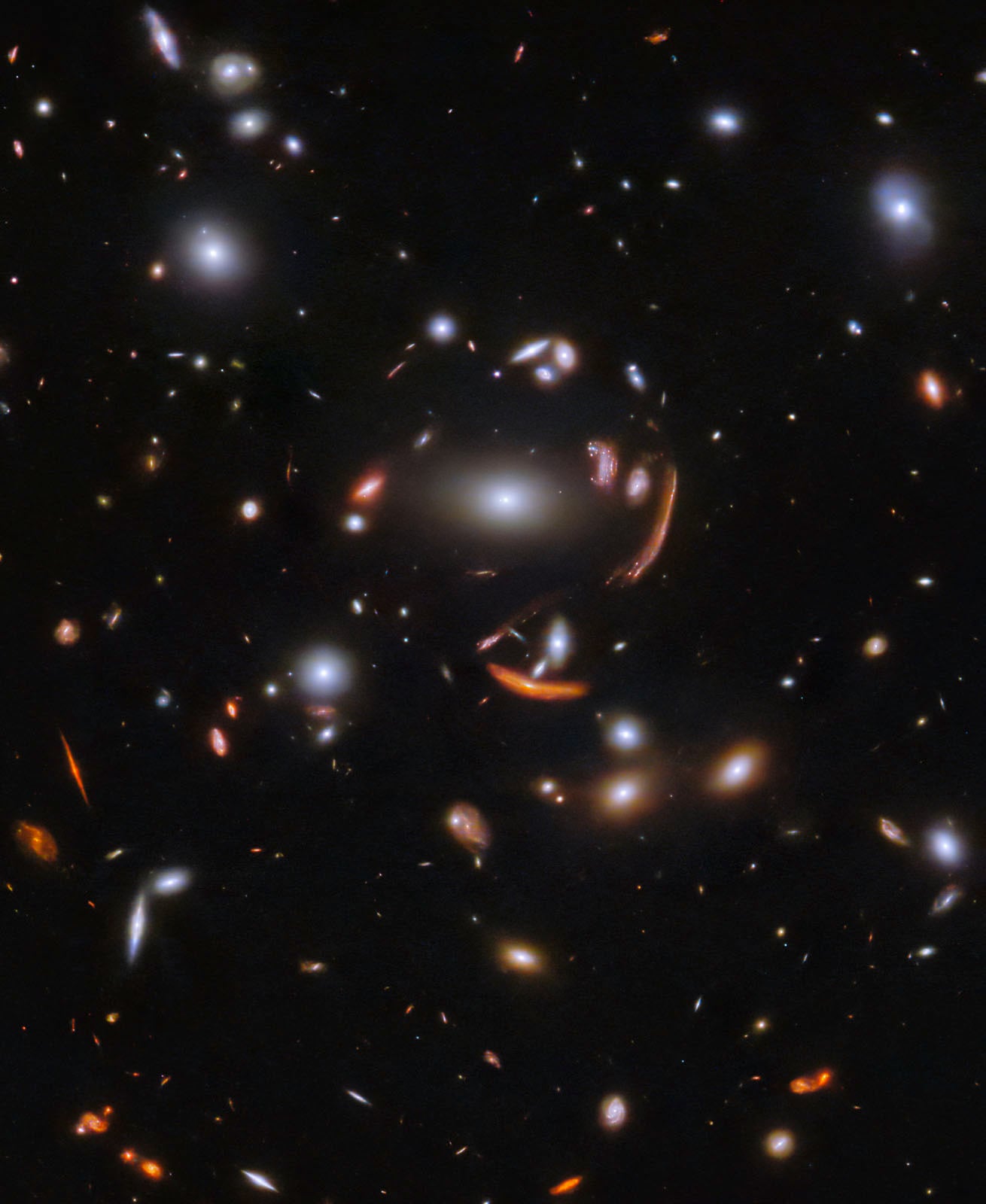 A deep space image shows numerous bright galaxies of various sizes and shapes against a dark background, with some galaxies stretched into arcs due to gravitational lensing.