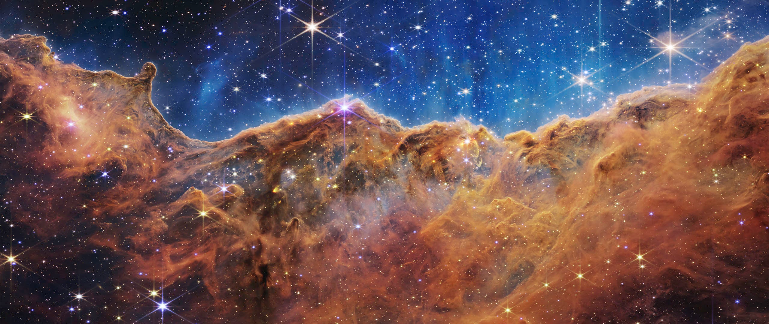 Colorful nebula with bright stars scattered across a vivid blue and orange cosmic cloud, resembling a mountainous landscape in outer space.