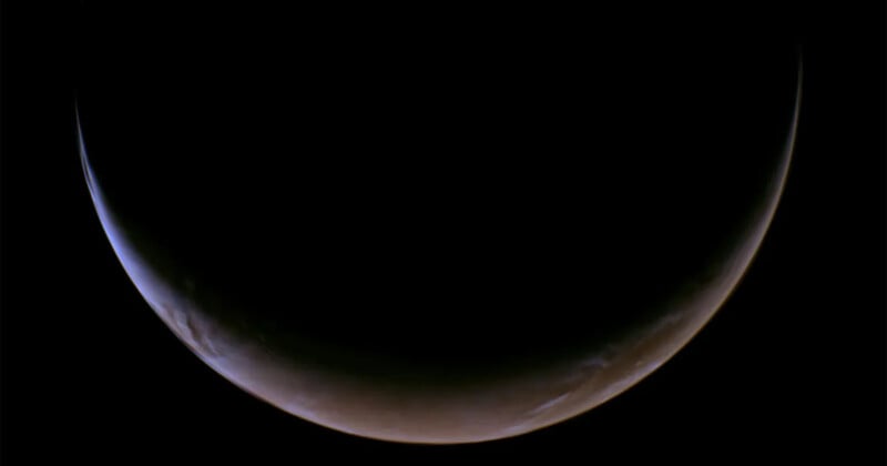 A dark, crescent-shaped planet is illuminated along its curved edge, with deep shadows obscuring most of its surface against a black background.