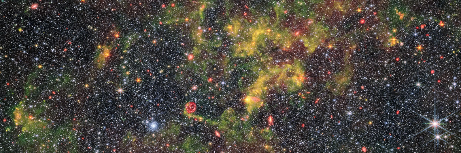 A dense field of stars fills the image, with areas of yellow-green nebula clouds and scattered reddish spots. A bright star shines near the bottom right. The scene shows the beauty of deep space.