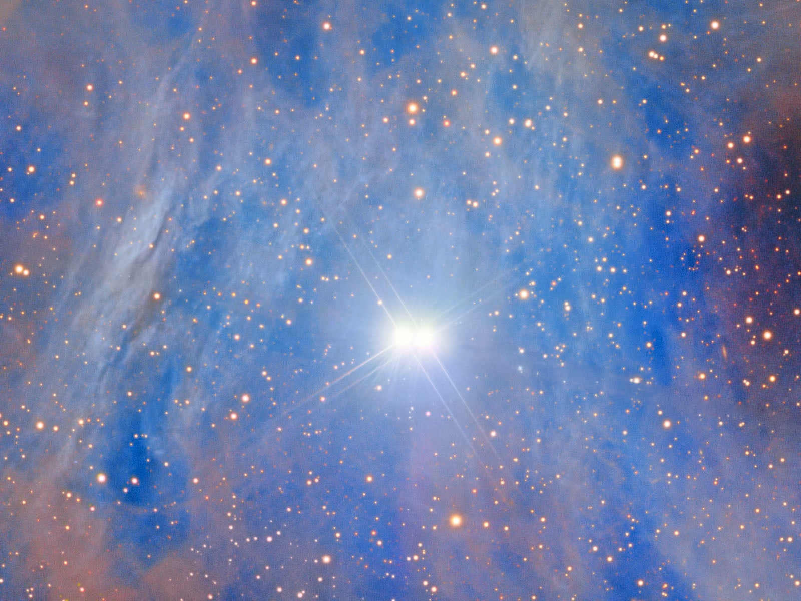 A bright star shines in the center of a blue-hued nebula, surrounded by numerous smaller stars against a dark, star-filled background.