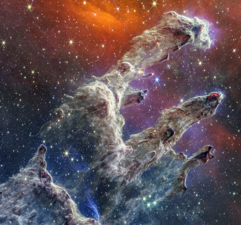 Three towering, finger-like columns of interstellar gas and dust, known as the Pillars of Creation, rise against a backdrop of colorful stars and glowing cosmic clouds in deep space.