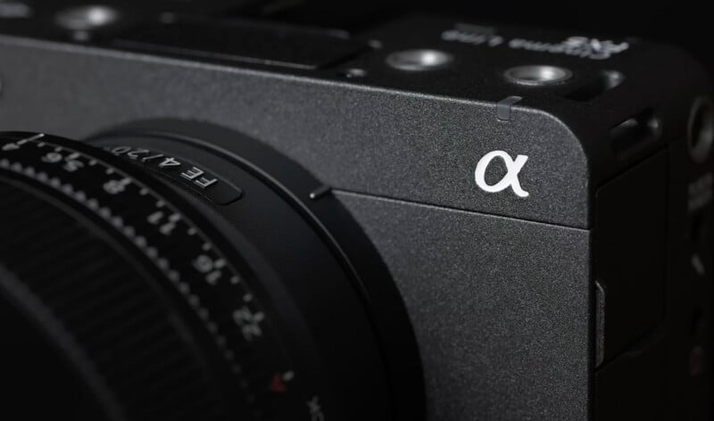 Close-up of a black Sony Alpha series camera, showing its textured body, lens details, and the white Alpha (α) logo on the front corner.