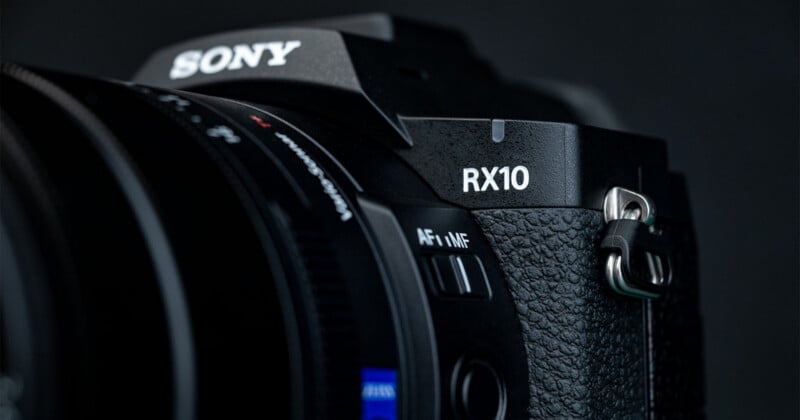 Close-up of a black Sony RX10 camera showing the textured grip, part of the zoom lens, focus mode switch, and the RX10 label against a dark background.
