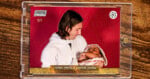 A trading card in a clear case shows a man in white holding a baby in pink, both against a red background. The card reads “LIONEL MESSI & LAMINE YAMAL” at the bottom. Top left text: “STADIUM Chrome 1/1.”.