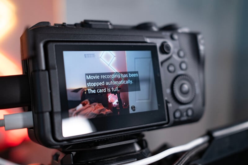 Close-up of a digital camera's screen displaying a message: "Movie recording has been stopped automatically. The card is full." A room with a bed and pink lighting is visible on the screen.