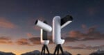 Two white, modern, robotic telescopes on tripods stand against a twilight sky with mountains in the background.