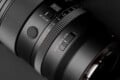 A close-up view of a camera lens barrel featuring an aperture ring with f-stop markings, an AF/MF switch, a customizable button, and a click on/off switch.