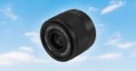 A black camera lens floating against a bright blue sky with scattered white clouds.