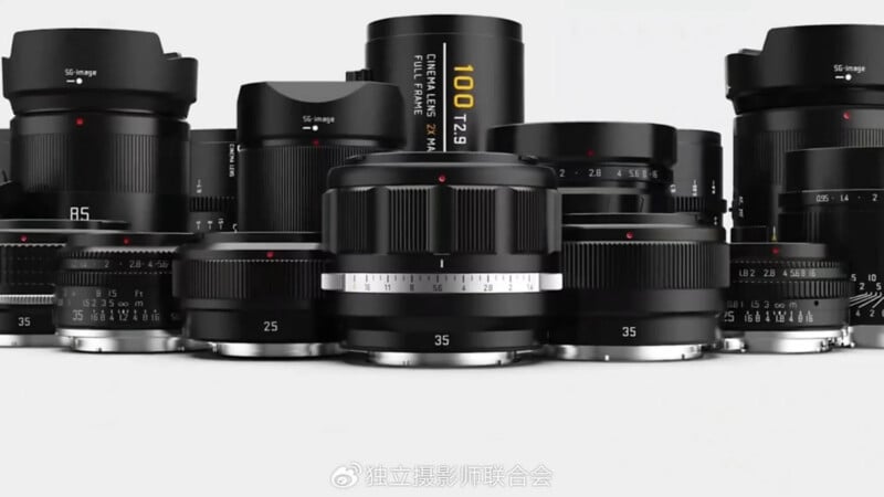A group of black camera lenses of various sizes and focal lengths, including 25mm, 35mm, 85mm, and a 100 T2.9, are arranged closely together on a white background.