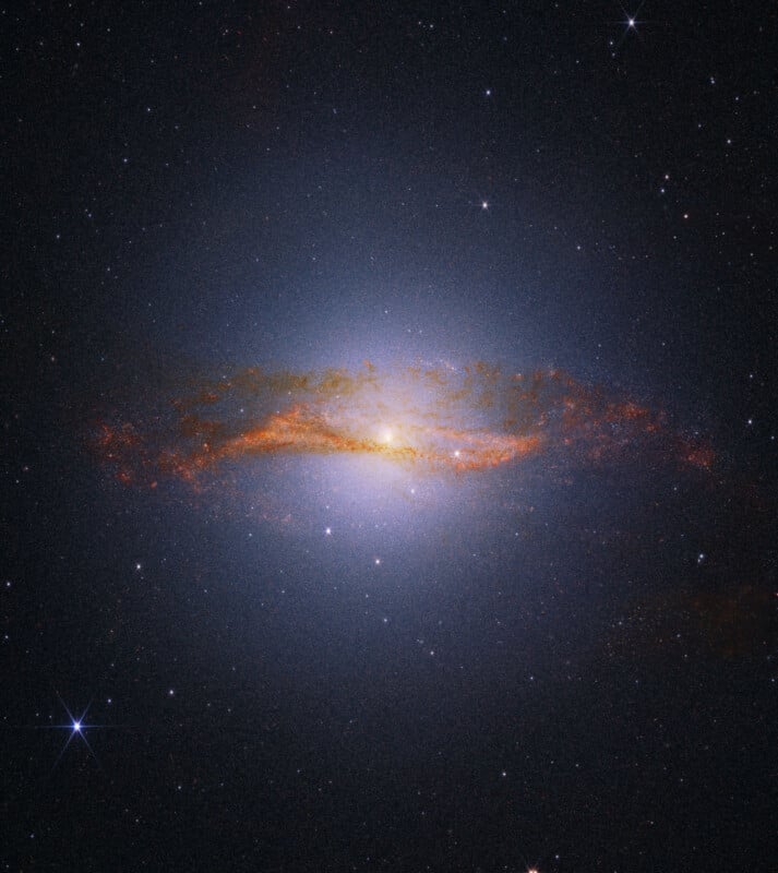 A bright spiral galaxy with a glowing center and orange-tinted dust lanes, surrounded by a dark star-filled space background.