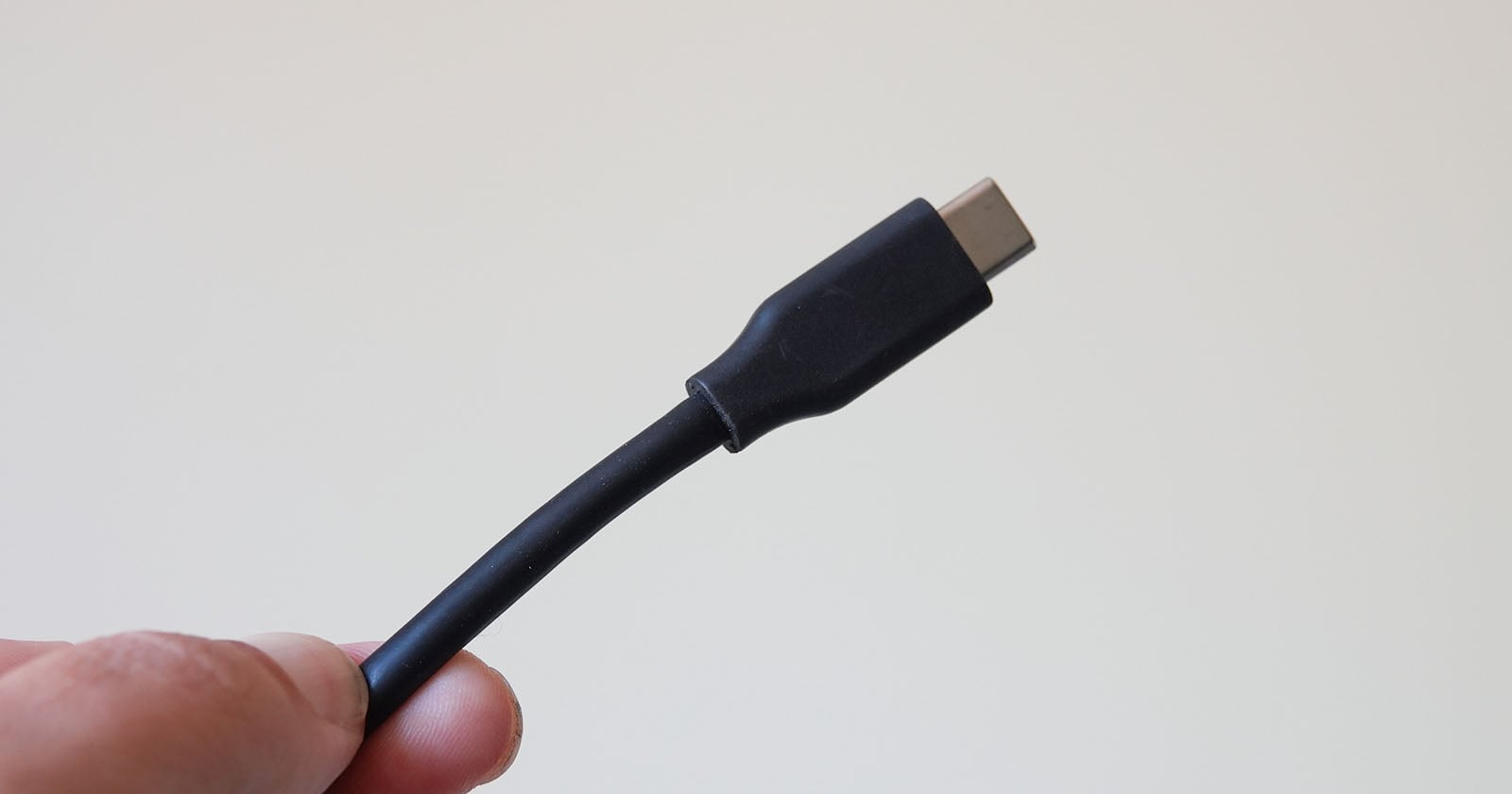 A hand holding a black USB-C cable against a plain light-colored background.