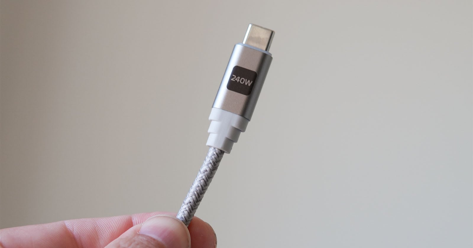 A hand holds a braided USB-C cable labeled "240W" against a plain, light-colored background.