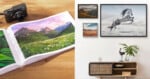 A photo book with landscape images lies open on a wooden table beside a camera. Nearby, framed nature and horse photos hang above a modern sideboard with decor items, including a plant and a bird sculpture.